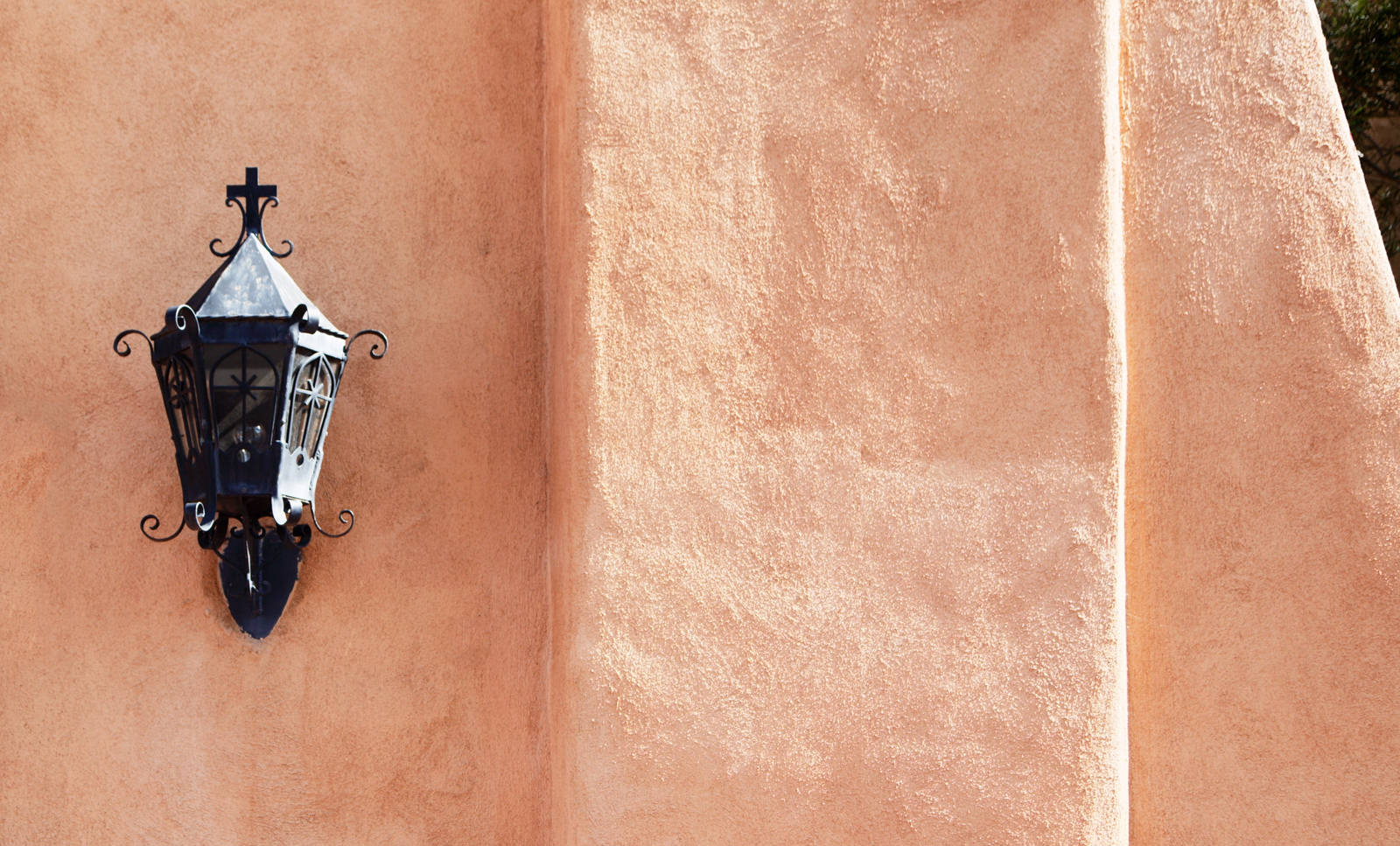 Entrance lamp with cross on sunlit adobe wall
